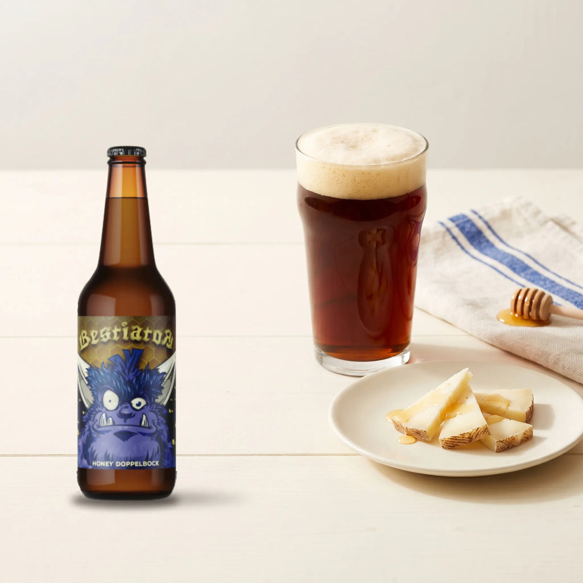 Bestiator - Cerveza Charra con MIEL – un vaso de cerveza con miel servido con una tapa de queso, y la botella al lado