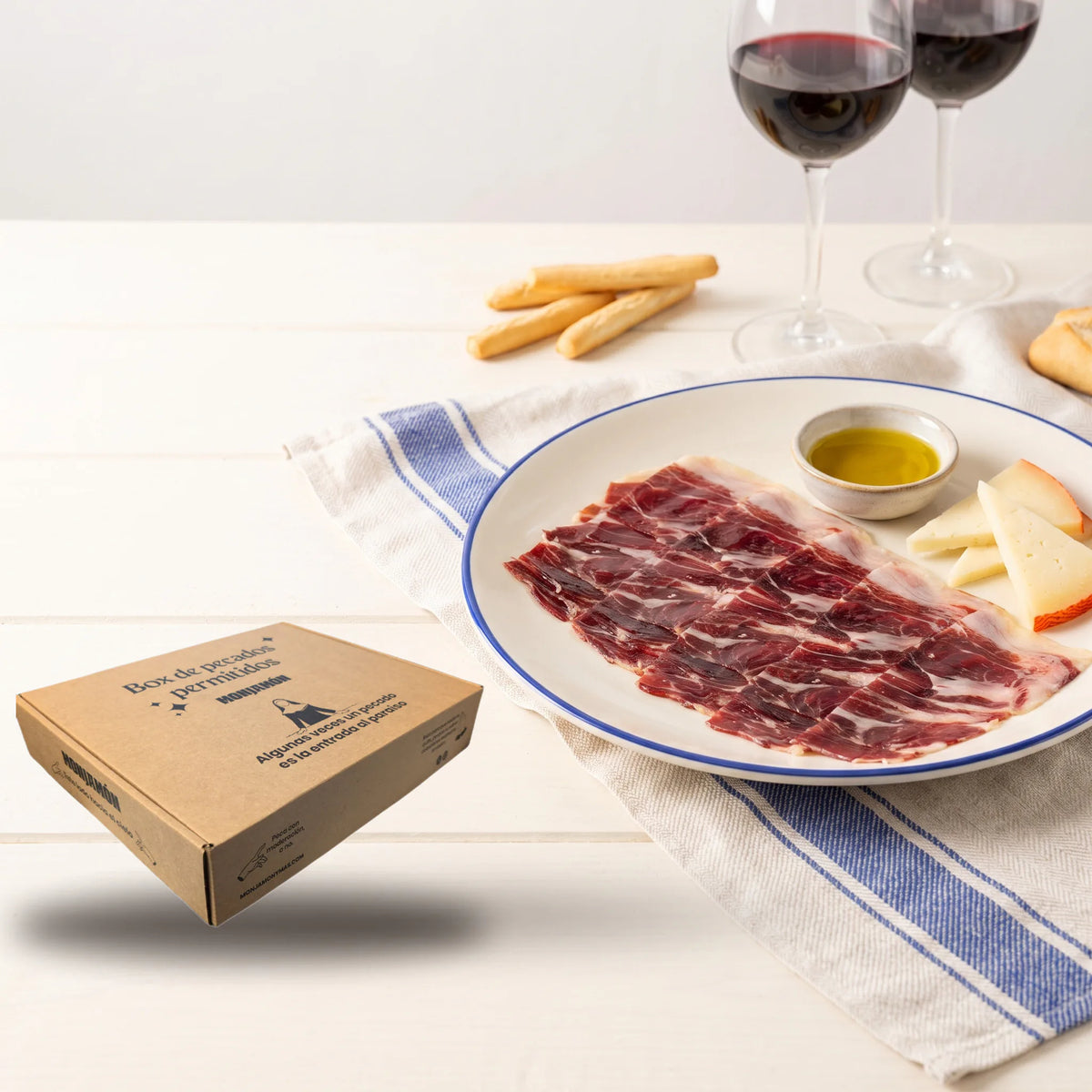 Cesta Caída del Cielo con Jamón de Bellota 100% Ibérico – la caja de la cesta junto a un plato de jamón, queso y aceite