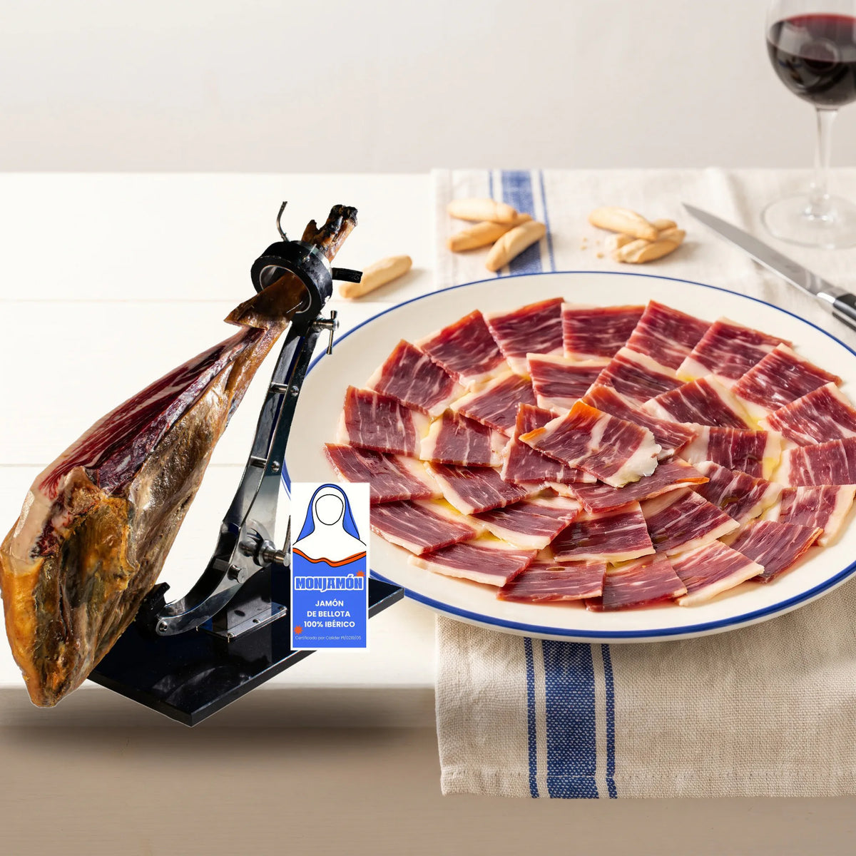 Jamón de Bellota 100% Ibérico +42 Meses · Certificado BRIDA NEGRA · Pieza grande 7-7,5kg – el jamón en su jamonero junto a un plato de jamón cortado a cuchillo