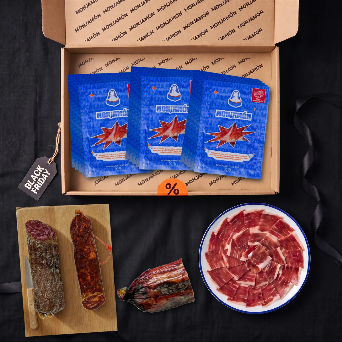 Pack Vicio · Black Friday – vista desde arriba: la caja con medio jamón de bellota 100 % ibérico +42 meses loncheado en 15 sobres, las 2 velas ibéricas de chorizo y salchichón en su tabla, la Divina Coppa entera y un plato de jamón