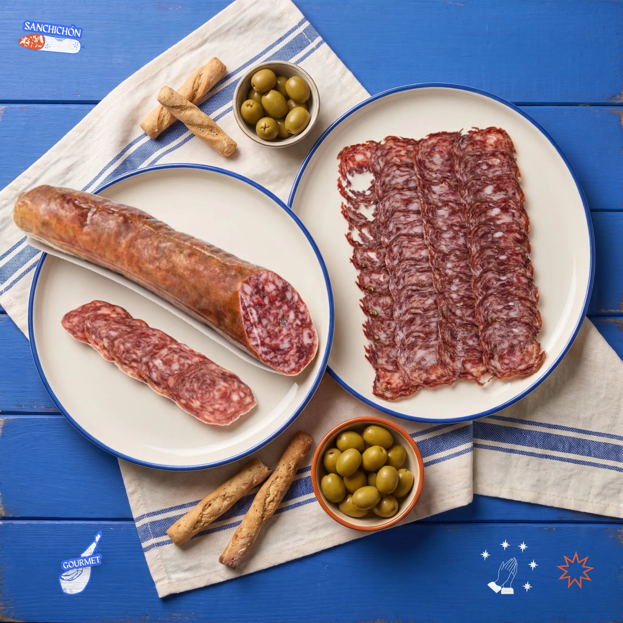 San chichón · Salchichón de Bellota 100% Ibérico · Media pieza 450-500 g – vista desde arriba: la media pieza de San Chichón junto a un plato de salchichón loncheado, picos y aceitunas