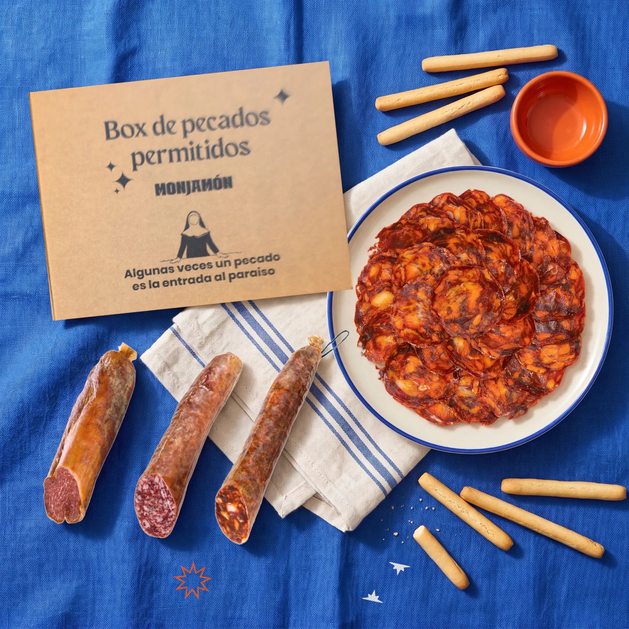 Surtido Embutido Ibérico de Bellota – vista desde arriba: la caja de cartón cerrada con el lomo, el salchichón y el chorizo al lado, y un plato de chorizo loncheado